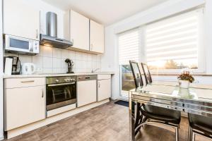 una cocina con armarios blancos y una mesa con sillas. en Ferienwohnung Köln Stammheim, en Colonia