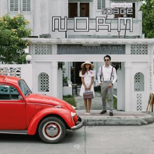 a man and a woman standing next to a red car at Norm Space Hostel NST in Nakhon Si Thammarat