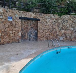 una piscina frente a una pared de piedra en La Rosa dei Venti Apts en Porto San Paolo