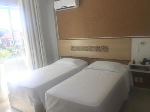 two beds in a hotel room with a window at Emirates Hotel & Suites in Santana do Livramento