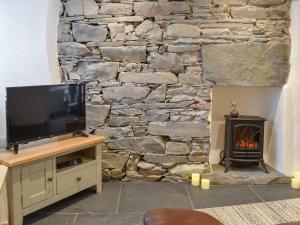 a living room with a tv and a stone wall at Ugly Duckling Cottage in Broughton in Furness