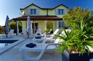 Casa amarilla con piscina y sillas blancas en Relax House Nizic, en Dražice