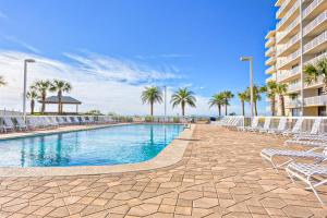 a swimming pool with chairs and palm trees and a building at Seaside Beach and Racquet Club Condos II in Orange Beach