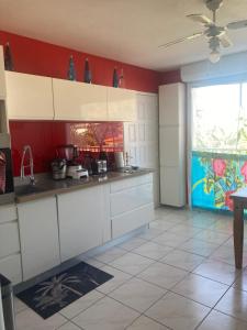uma cozinha com armários brancos e uma parede vermelha em Martinique trois ilets face à la mer em Les Trois-Îlets