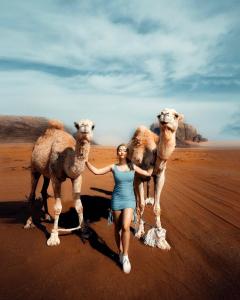 a woman is standing with two camels on the desert at Quite bedouin life in Wadi Rum