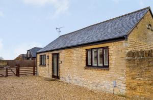 a brick building with a black roof and a fence at Coursehill Barn in Witney