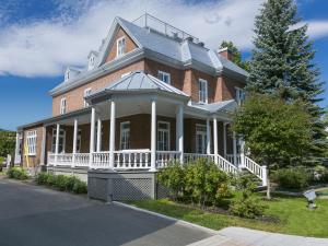 une grande maison en briques rouges avec une terrasse couverte blanche dans l'établissement 338 - Le Quai des Veuves - Les Immeubles Charlevoix, à Baie-Saint-Paul