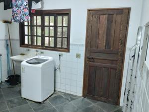 een badkamer met een wasmachine, een wastafel en een deur bij Casa à 250m praia Martim de Sá, quiosques, restaurantes e lazer in Caraguatatuba