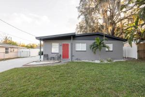 a gray house with a red door and a yard at EntireHouse w/Bush Garden View_Private Heated POOL in Tampa