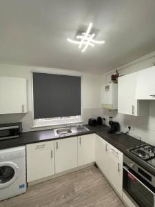 uma cozinha com armários brancos e um balcão preto em Spacious, Modern 2 Bed Apartment em Londres