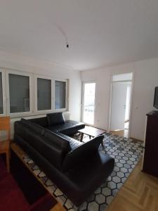 sala de estar con sofá de cuero negro y ventanas en Delux Apartment, en Sarajevo