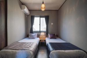 2 Betten in einem kleinen Zimmer mit Fenster in der Unterkunft プライベートハウス ぅーじ家 in Hanagusuku