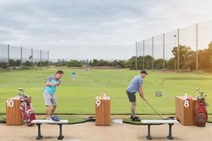 dos hombres están jugando golf en un campo de golf en The Retreat West Beach Parks, en Adelaida