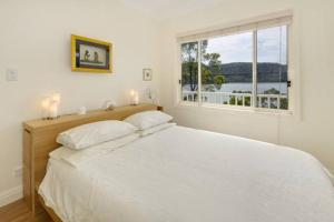 a white bedroom with a large bed and a window at Cosy Cottage Above the Hawkesbury w/ Jetty in Mooney Mooney