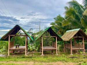 two huts with benches in a field with palm trees at Felcordz Nature Farm & Resort 
