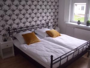 Una cama con sábanas blancas y almohadas amarillas en un dormitorio en House Louise. en Risum-Lindholm