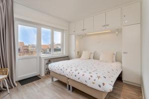 a white bedroom with a bed and a window at Flat Julien in De Panne