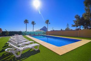 a row of white lounge chairs next to a swimming pool at Villa Ambar - PlusHolidays in Calpe