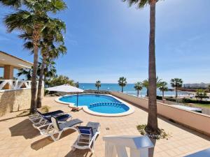 a swimming pool with chairs and palm trees and the ocean at Frontline Beach Villa Playa Flamenca in Orihuela