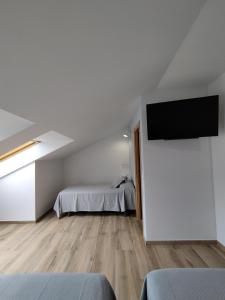a white bedroom with a bed and a flat screen tv at Pensión Residencial Platas in O Pedrouzo