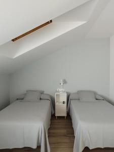 2 łóżka w pokoju z białymi ścianami i drewnianą podłogą w obiekcie Pensión Residencial Platas w mieście O Pedrouzo