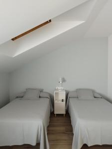 two beds in a room with white walls and wooden floors at Pensión Residencial Platas in O Pedrouzo