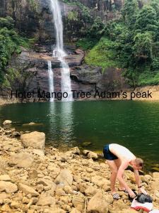a woman bending over on the rocks near a waterfall at Hotel mango tree nearest Adam's peak in Adams Peak