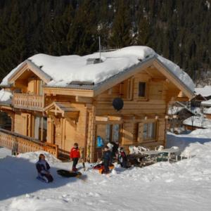 un grupo de personas en la nieve frente a una cabaña de madera en Chalet Tho'max, en Châtel