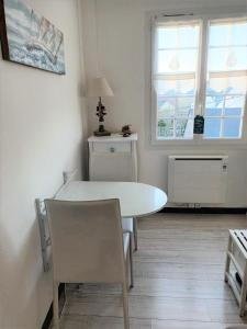 un comedor blanco con una mesa blanca y 2 ventanas en LE PETIT CABOURG de LA COUR NORMANDE Studio coeur de ville -1 à 2 personness, en Cabourg