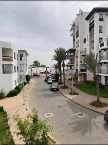een straat met geparkeerde auto's en palmbomen naast gebouwen bij Apartement Marina Zina, Agadir in Agadir