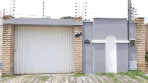 un garage avec une porte blanche et un bâtiment en briques dans l'établissement Cantinho arretado da Peste - Casa, à Aquiraz