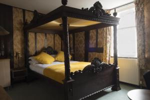 a bedroom with a wooden canopy bed with yellow sheets at The Sun Hotel in Canterbury