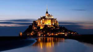 a castle on an island in the water at night at Maison au pied du Mont Saint Michel 2 in Pontorson