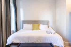 a bed with white sheets and yellow pillows and a window at Thena Hotel - Large Studio in Philadelphia