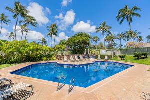 a swimming pool with chairs and palm trees at Kuilima Estates East 41 - Plumeria Tree House in Kahuku