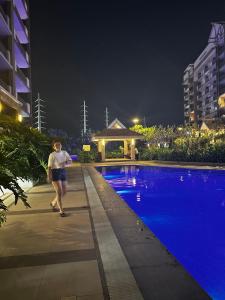 a woman walking by a swimming pool at night at Alea Residences in Manila