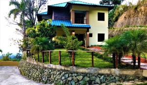 une maison sur une colline avec une clôture devant elle dans l'établissement Green Village By Hospedify, Hermosa Villa En Las Alturas con Piscina, Billar, y BBQ, à Jarabacoa