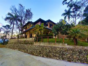 une maison avec un mur en pierre et des palmiers dans l'établissement Green Village By Hospedify, Hermosa Villa En Las Alturas con Piscina, Billar, y BBQ, à Jarabacoa