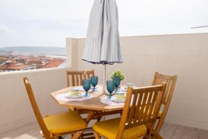 een eettafel met stoelen en een parasol bij Olhos d'Água - Penthouse in Nazaré
