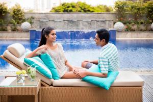Ein Mann und eine Frau sitzen auf einer Couch neben einem Pool in der Unterkunft Fairfield by Marriott Bengaluru Outer Ring Road in Bangalore