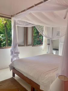 a bedroom with a white canopy bed with windows at Pousada Loin de Tout in Corumbau