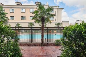 a building with a fence and a palm tree in front of a pool at Courtyard Shreveport-Bossier City/Louisiana Boardwalk in Bossier City