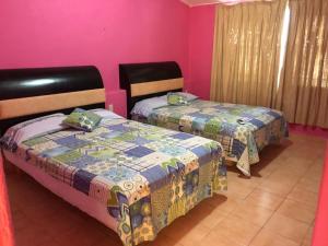2 Betten in einem Zimmer mit rosa Wänden in der Unterkunft Hermosa Casa Ikal en Acapulco in Barra de Coyuca