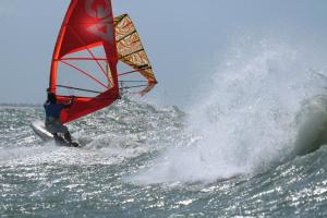 a person on a surfboard with a sail in the ocean at Casa de Lala Beach House in São Miguel do Gostoso