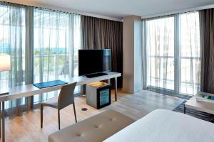 Habitación de hotel con escritorio, TV y ventanas grandes. en AC Hotel by Marriott Miami Beach, en Miami Beach