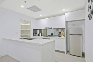 a white kitchen with white cabinets and a refrigerator at Aircabin｜Mascot｜Spacious & Modern｜Walk to station in Sydney