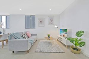 a white living room with a couch and a tv at Aircabin｜Mascot｜Spacious & Modern｜Walk to station in Sydney