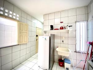 a white tiled kitchen with a sink and a refrigerator at 202 Kitnet no centro com wifi in Aracaju