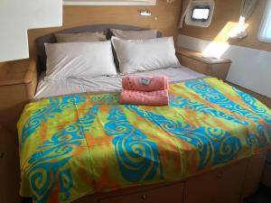 1 cama grande con edredón colorido y 2 toallas rosas en Catamaran Apetahi en Uturoa