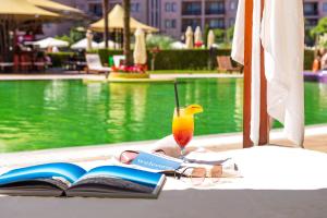 a book and a drink on a table next to a pool at Barcelo Royal Beach - All Inclusive in Sunny Beach